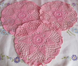 Three pink crochet doilies on embroidered mat