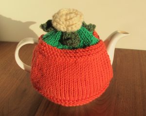 Tea cosy in terracotta colour with white flower and leaves on top