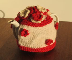 White tea cosy with red stripe at top and bottom and red and white flowers on body and top