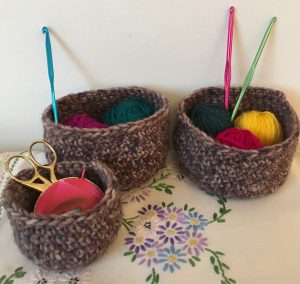 Three tweedy crocheted baskets holding wool and crochet hooks