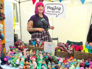 Hanks of colourful HeyJay yarn on a stall with the pink-haired owner behind them