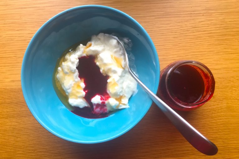 Overhead shot of blue bowl of yogurt, compote and honey with jar of blackberry compote